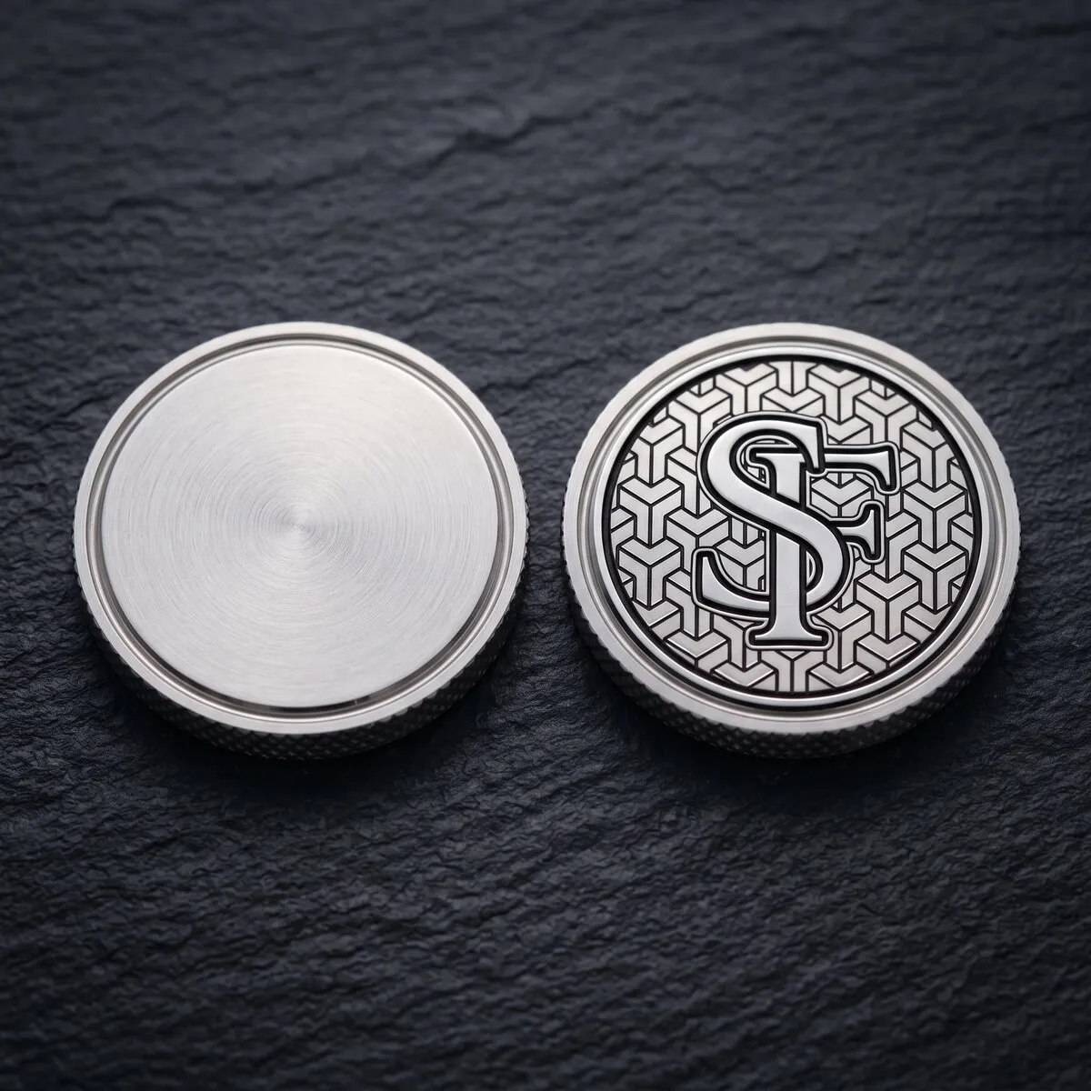 Zwei Ballmarker aus Edelstahl auf Schiefer: links ein blanker Rohling, rechts derselbe Marker mit graviertem SF-Monogramm auf Würfelmuster