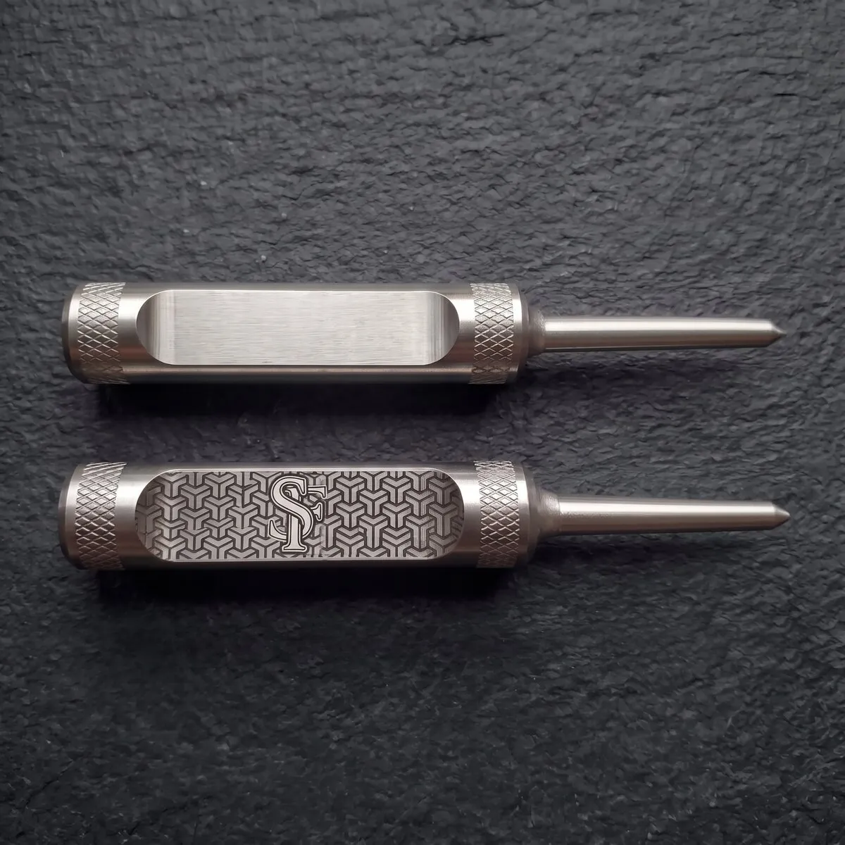 Zwei Divot Tools aus Edelstahl mit gerändeltem Griff und Stift, von oben: oben die blanke gefräste Fläche, unten dieselbe Fläche ganz graviert mit SF-Monogramm und Würfelmuster